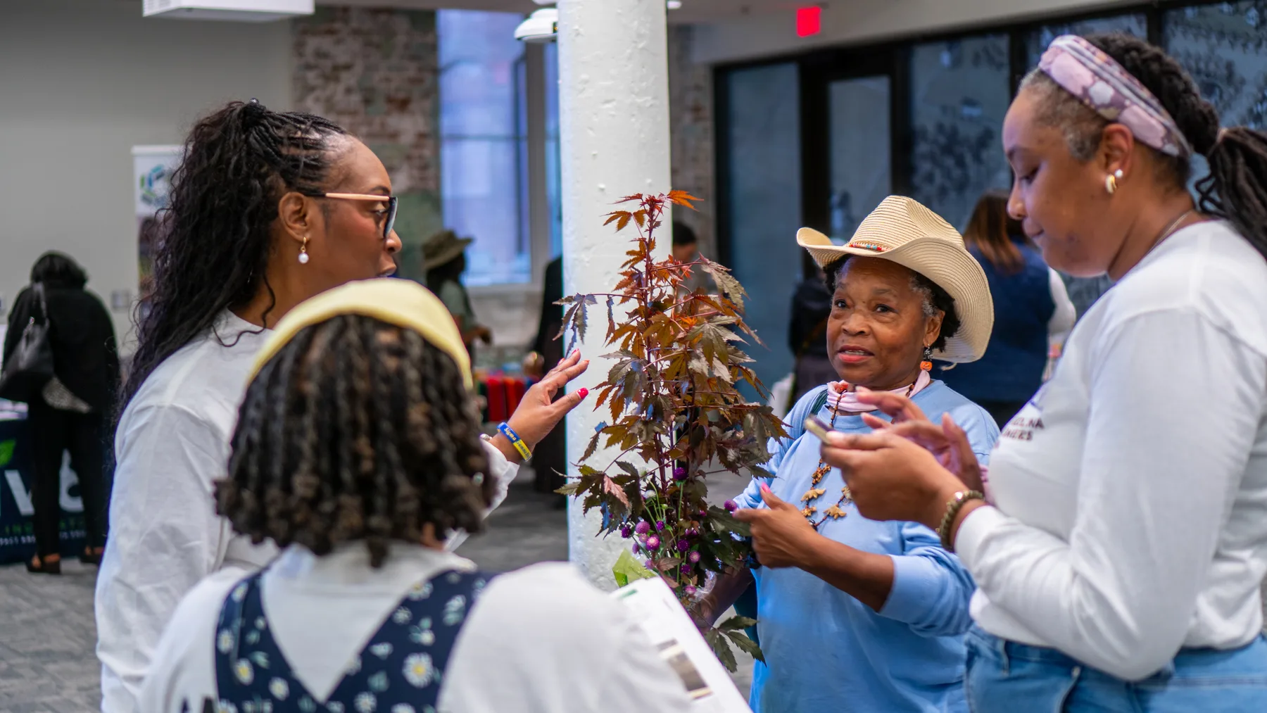A young person in a wide-brim hat receives a potted plant from an adult.
